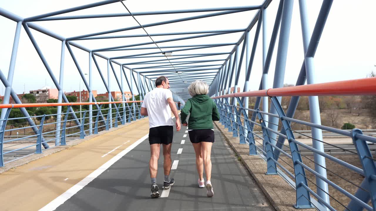 Pareja mayor feliz trotando y celebrando en un puente moderno