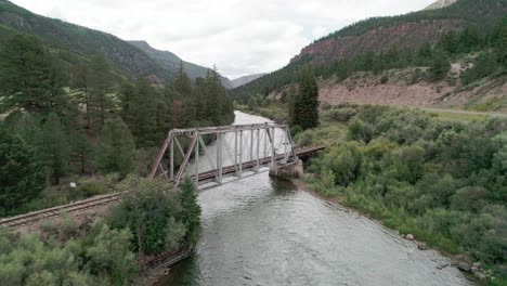 vista de drones de un puente con un ferrocarril que pasa sobre un río en el campo colorado