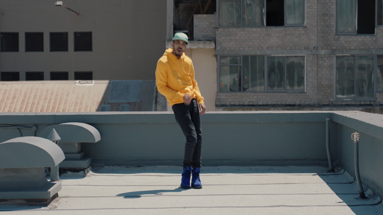 춤추는 남자  ⁇ 합 댄서가 노란색 후디를 입고 도시의 옥상에서 프리스타일 댄스 동작을 수행합니다.