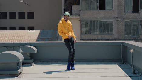 Hombre-Bailando-Bailarín-De-Hip-Hop-Realizando-Movimientos-De-Baile-De-Estilo-Libre-En-La-Azotea-De-La-Ciudad-Con-Sudadera-Con-Capucha-Amarilla