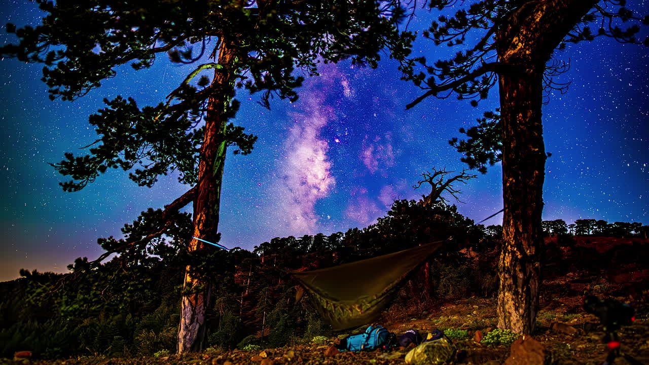 hamaca entre los árboles bajo el cielo nocturno con estrellas y galaxias en movimiento