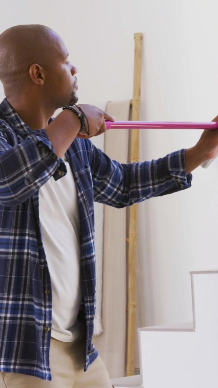 Video verticale: Uomo in camicia di flanella blu che tiene uno strumento rosa e preme la parete della scala vicino al corrimano.