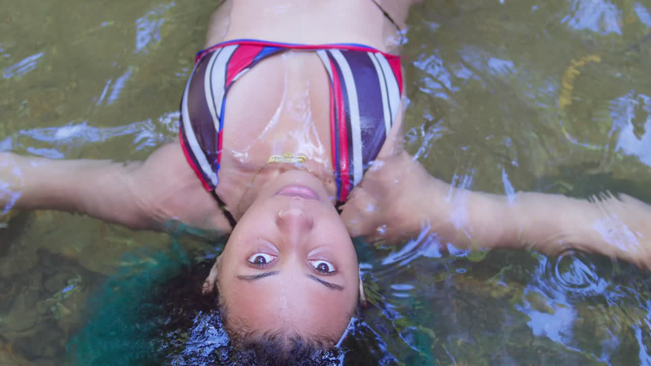 A young woman in a sexy bikini floats in the crystal clear waters of a river on a tropical island