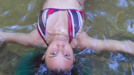 a young woman in a sexy bikini floats in the crystal clear waters of a river on a tropical island