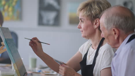 an old retired woman paints a picture together with friends. an elderly group of friends and a senior woman are drawing pictures together.