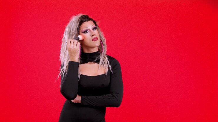 Drag queen che si trucca con un pennello su sfondo rosso
