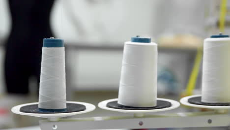 closeup of three big bobbins with thin white thread on working professional sewing machine. real time full hd video footage