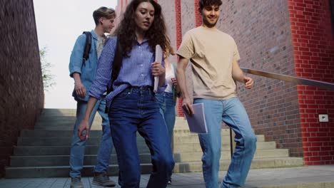 Three-caucasian-students-walking-down-the-stairs-at-university-campus.