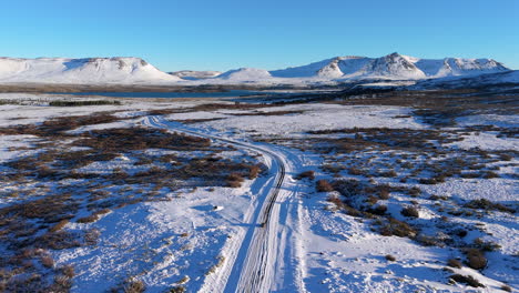Forward moving drone frames a snowy Caviahue landscape in Patagonia as a lone car follows a winding road toward volcanic peaks and a blue lake under crisp winter light
