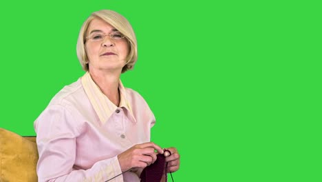 mujer mayor alegre tejer y escuchar a una persona detrás de la cámara en una pantalla verde, clave de croma