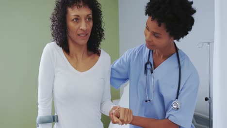 vista frontal de una mujer médica afroamericana ayudando a una paciente a caminar en la sala del hospital