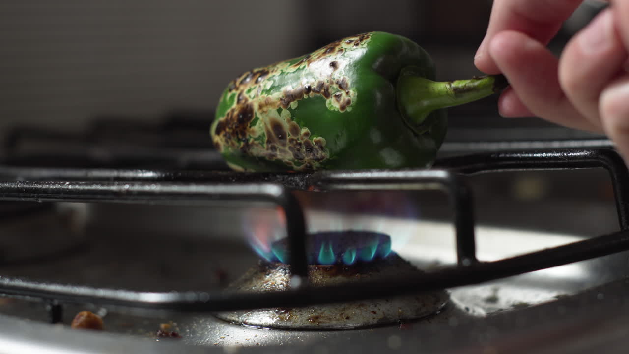 mano girando pimiento verde asado sobre el fuego de la estufa en la cocina