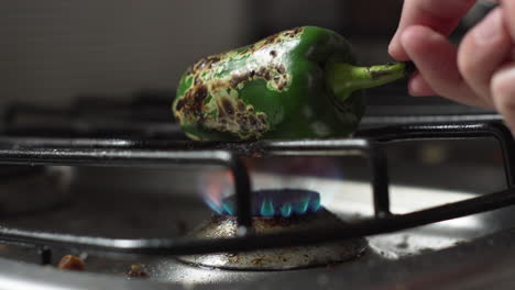 hand turning green bell pepper roasting over stove fire in the kitchen