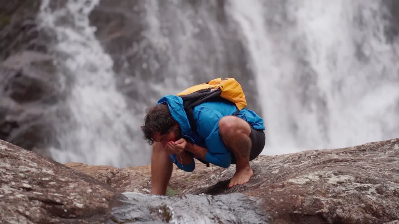 Barefoot man drinks water from natural stream near waterfall in Minas Gerais, Brazil