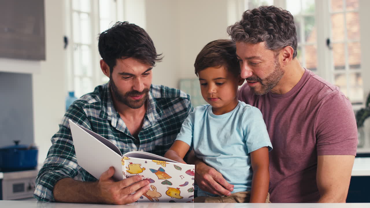 familia del mismo sexo con dos padres e hijo leyendo un libro en la cocina en casa juntos
