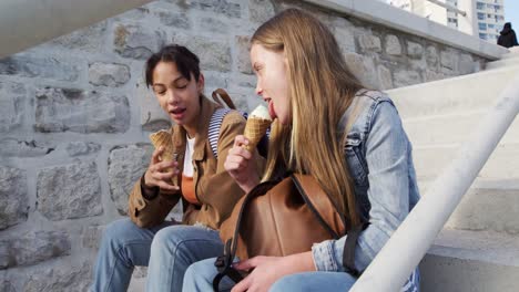 side view of a caucasian and a mixed race girl eating sitting on stairs