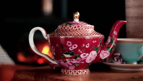 beautiful red oriental tea pot with bird and flower design on a table with a fire burning behind