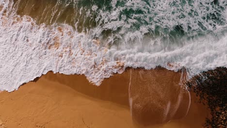 Toma-Cenital-De-Una-Hermosa-Ola-Rompiendo-En-La-Mágica-Playa-De-Arena,-Ericeira,-Portugal