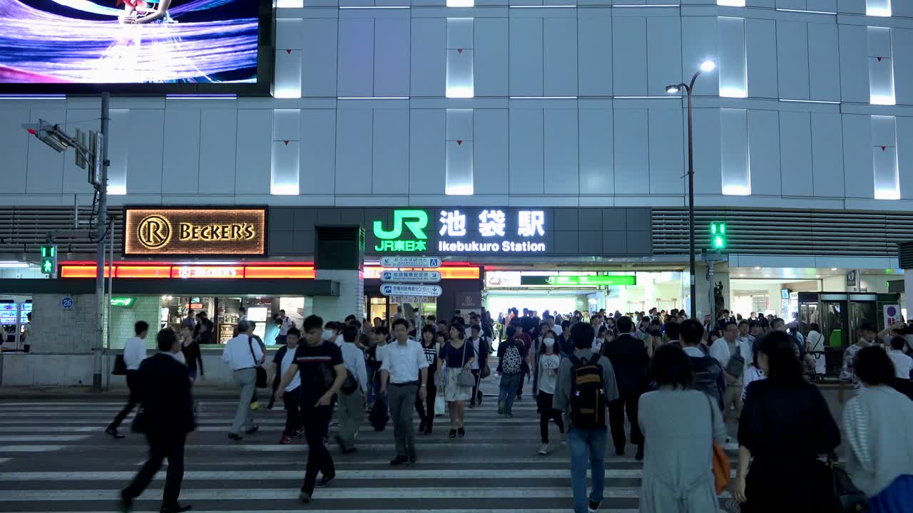 Night scene of a busy Ikebukuro Station in Tokyo, Japan, with JR East signage and many people.
