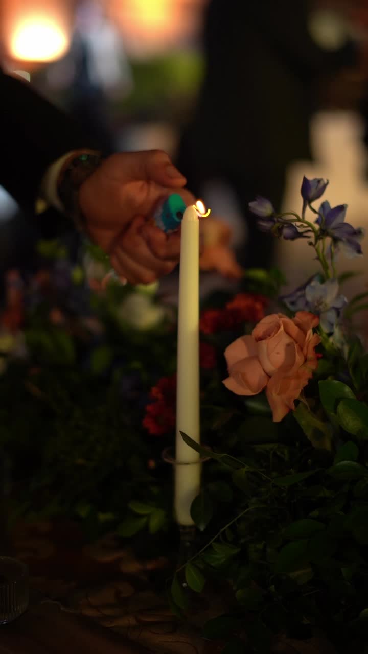 Un cameriere accende una candela bianca con un fiammifero durante una cena romantica, primo piano, inquadratura d'inserto.