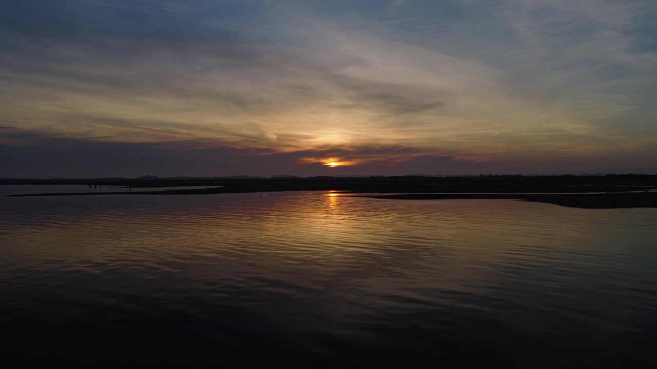 Wadden Sea near Terschelling, Friesland, Netherlands, revealing calm tidal waters, sunset reflection, expansive tidal flats and evening sky, drone forward flyover.