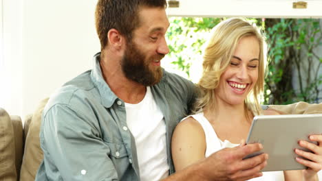 cute couple sitting on a sofa looking a tablet