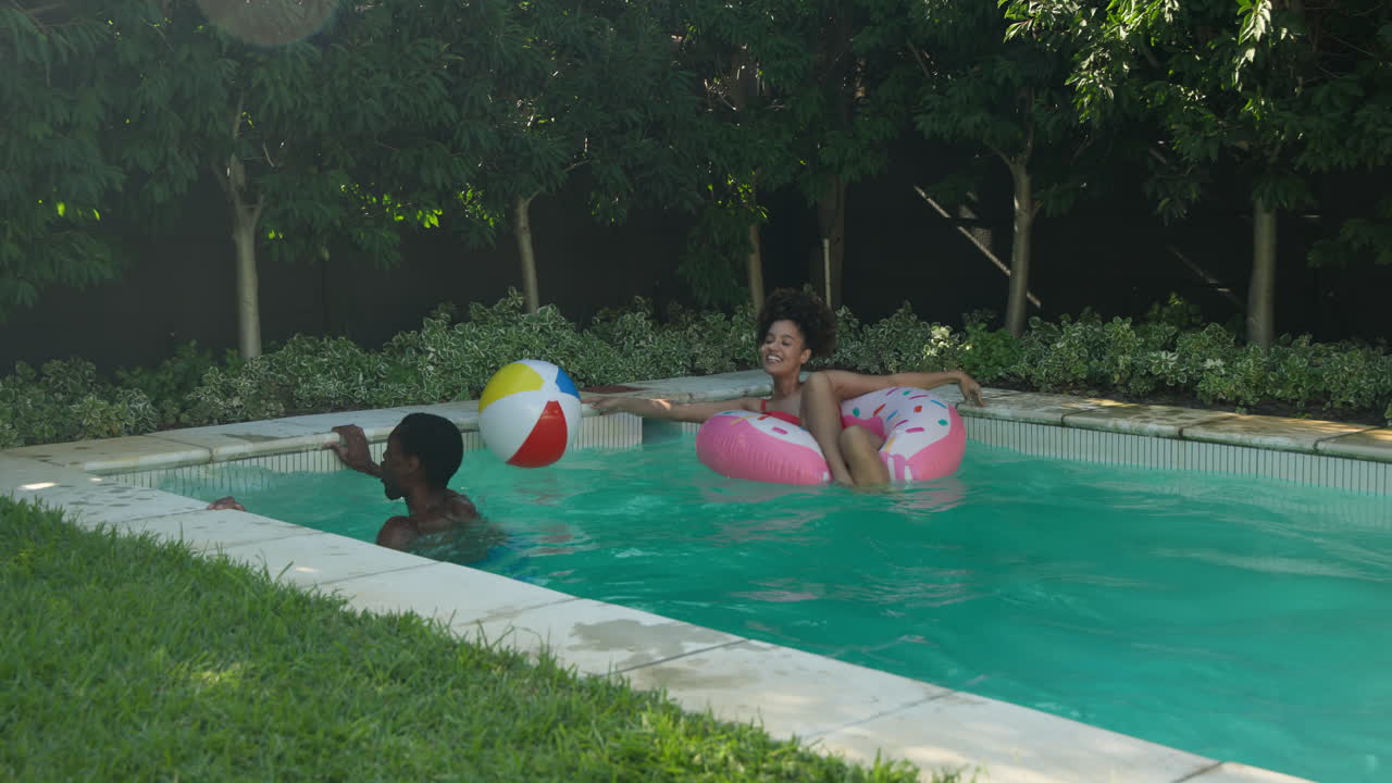 Diverse friends enjoying pool day, woman on float laughing, man tossing beach ball