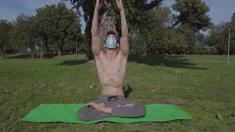 Young-caucasian-man-with-mask-practicing-yoga-at-outdoor-place