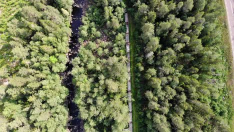 Toma-Aérea-Siguiendo-La-Ruta-De-Los-Escalones-De-La-Escalera-De-Salmón-Dentro-Del-Bosque-De-Coníferas-Siempre-Verde-Que-Conduce-A-Una-Presa-De-Agua-En-Una-Zona-Rural-Remota-En-Suecia