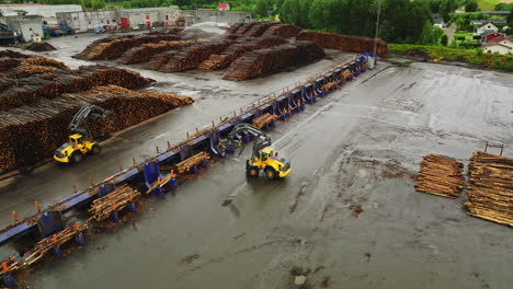 log loaders in braskereidfoss move among massive piles of timber logs, aerial