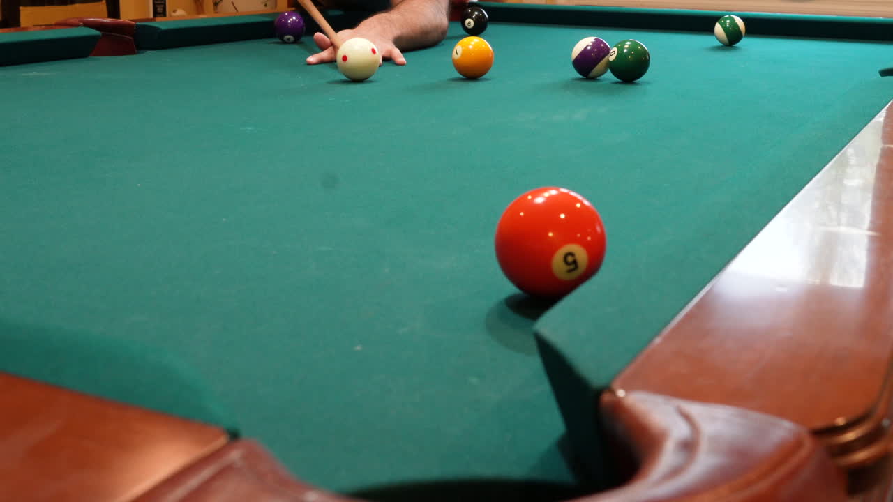 Man Playing 8 Ball Pool Shoots Solid 5 and 1 Balls into Pockets on a Brunswick Table with Green Felt and Several Balls Left on the Table, Open Bridge Hand and Wooden Cue Stick, Low Angle no faces