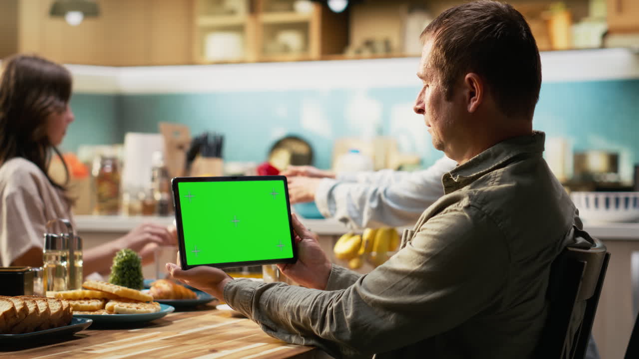 Green screen on tablet next to parents and girl sharing breakfast in home kitchen