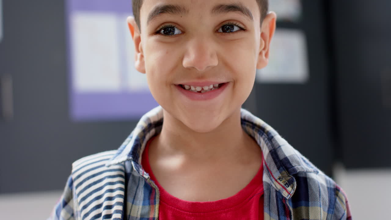 Smiling boy in school classroom wearing plaid shirt and red t-shirt