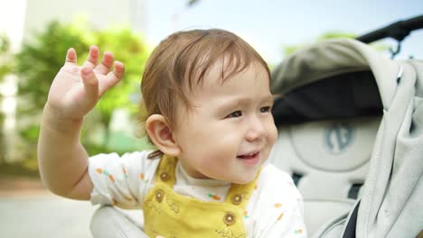 Happy-little-cute-adorable-baby-girl-waving-hand-with-a-toothy-smile-positive-face-expression-while-sitting-in-the-stroller-or-pushchair