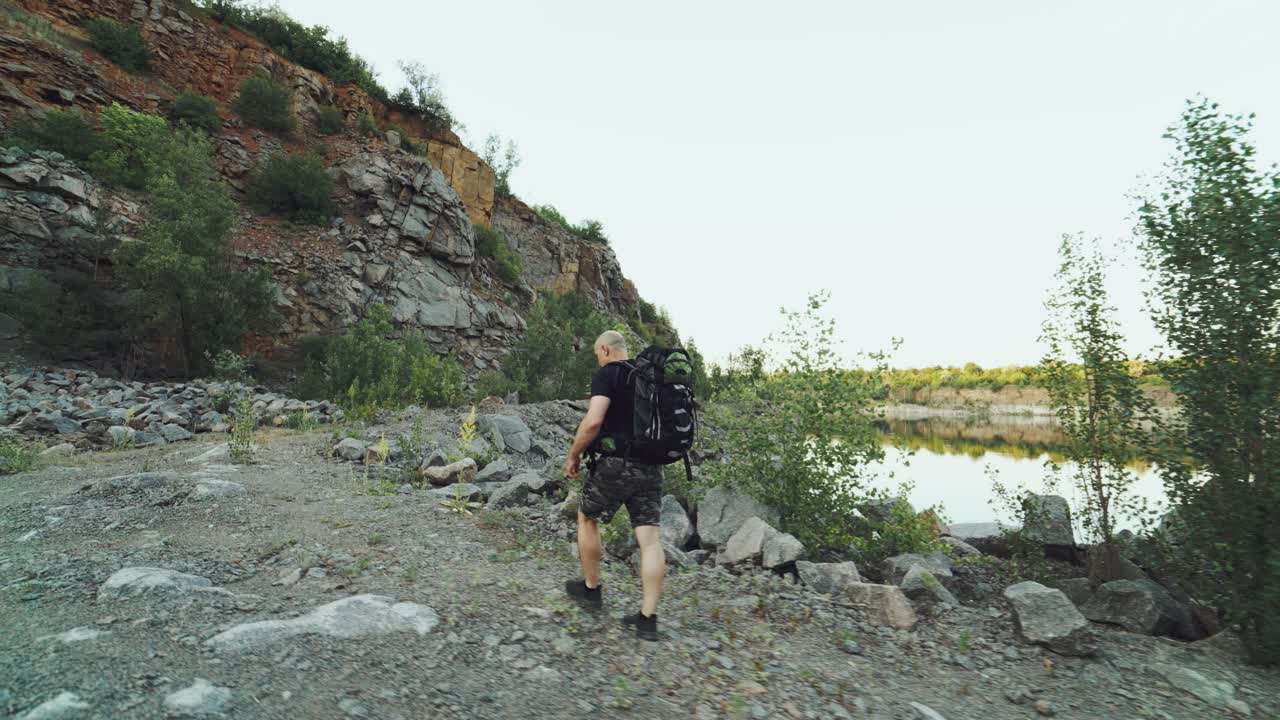 traveler in comfortable clothes and in running shoes is walking at the edge of a river near the rocks on the background of a beautiful view in the summer