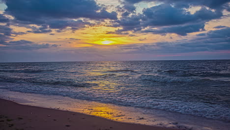 Clouds-float-calmy-in-sky-as-sun-sets-yellow-light-over-calm-ocean-waves