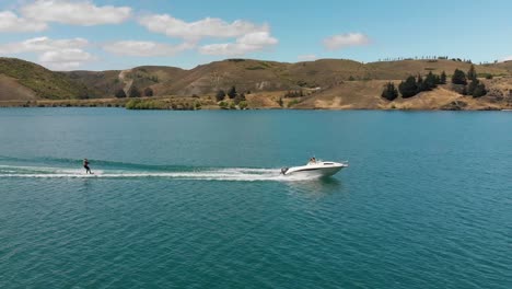 esquí acuático detrás de un barco en el lago dunstan cerca de la represa clyde, otago central, nueva zelanda con montañas y nubes en el fondo