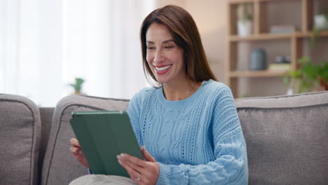 mujer sonriendo y usando una tableta en un sofá