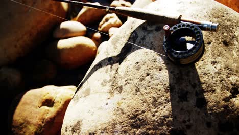 caña de pesca con mosca, carrete y gancho en roca