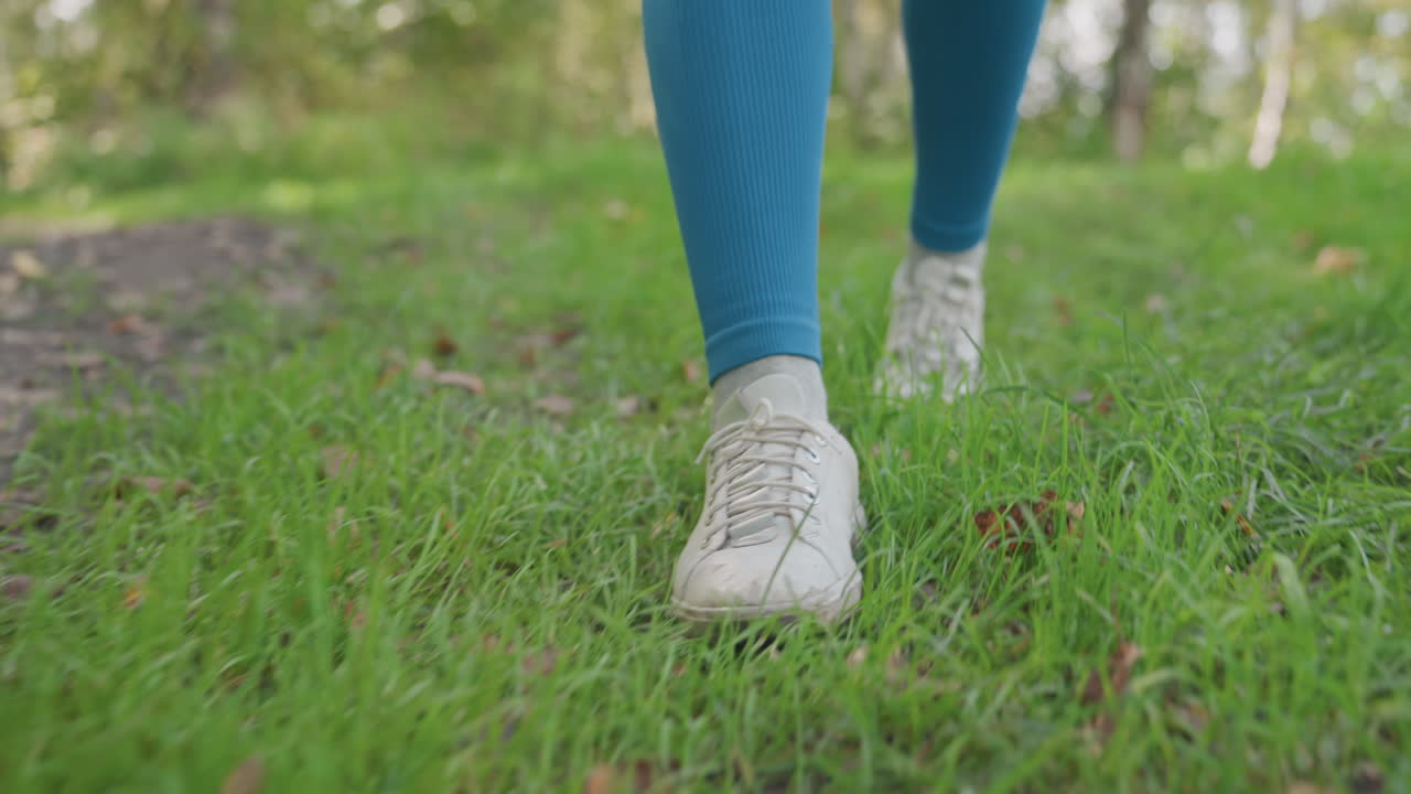 She carefully moves across damp grass. Female slowly advances through moist outdoor environment with attention. Woman navigates carefully through moist and wet outdoor grassy landscape