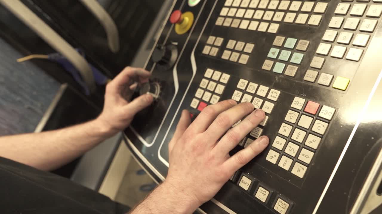 Operatore di macchine regola le impostazioni su un pannello di controllo CNC utilizzando tastierino e selettore rotante. Controllo della produzione industriale all'interno di uno stabilimento di produzione.