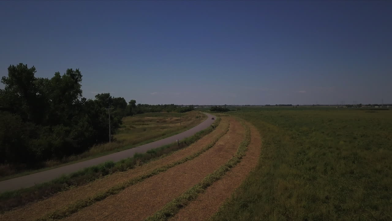 Drone shot of wide land towards road covered by trees under clear sky in the summer