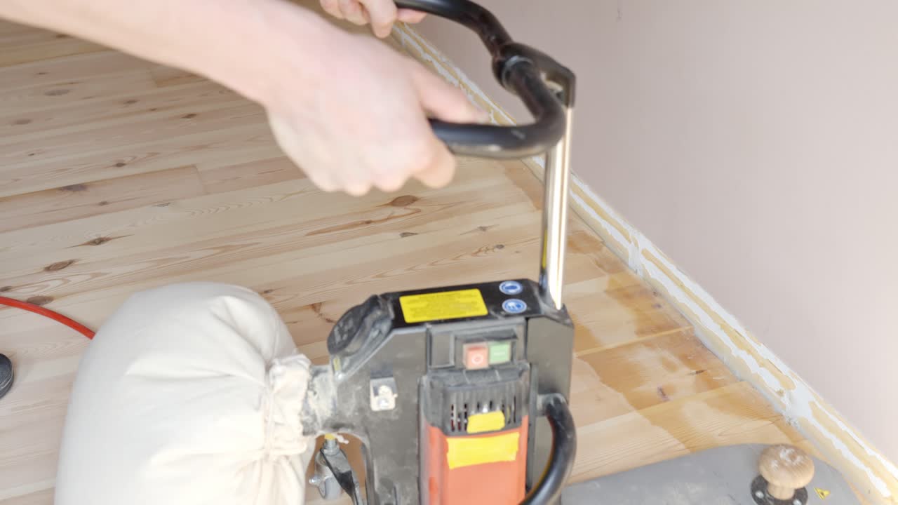 Man sanding wood floor edges with edge sander in bright indoor room