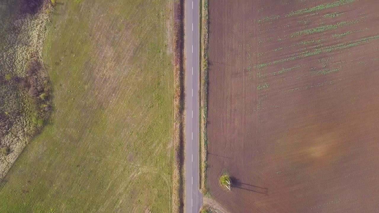 Flying over a road in a rural with a few cars looking down from a drone