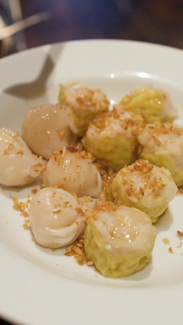Potret close-up tangan menggunakan sendok untuk menaburkan bawang putih goreng ke atas dim sum.