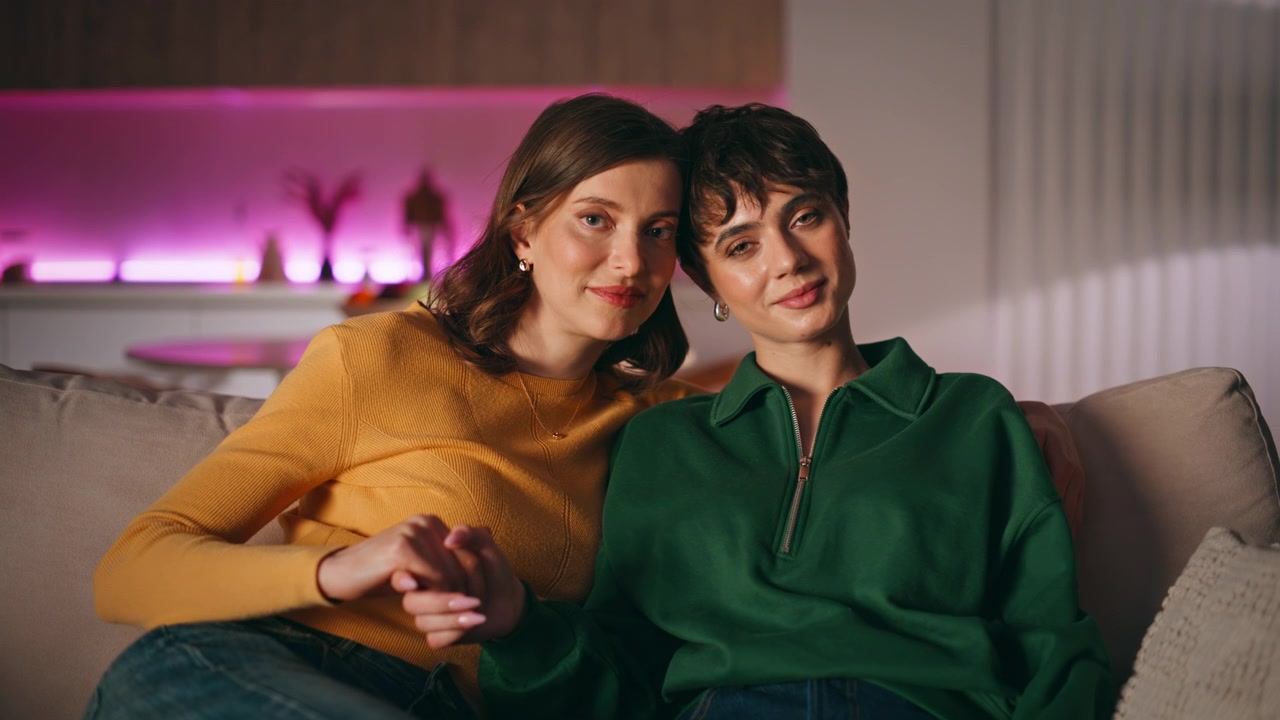 Lgbtq partners holding hands sitting couch looking each other with love closeup.