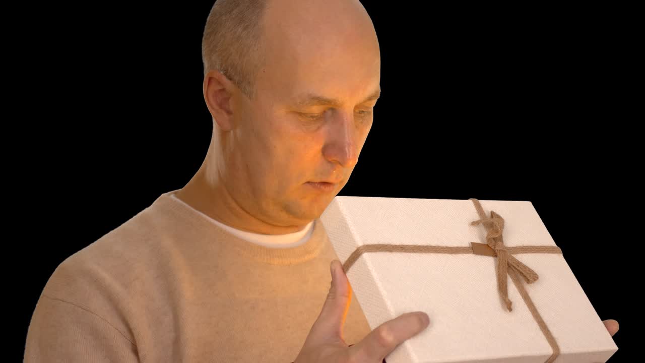 행복한 성인 백인 남자는 선물 상자를 얻습니다. 남자는 카메라를 보고 미소 짓고 있습니다. 얼굴에 오렌지색 빛이 있습니다. 손에 마법의 선물. 전면 뷰. 남자는 말합니다. 알파 채널 크로마 키 투명한 배경.