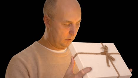 hombre caucásico adulto feliz recibe una caja de regalos. hombre mirando a la cámara y sonriendo. luz naranja en su rostro. regalo mágico en las manos. vista frontal. hombre hablando.