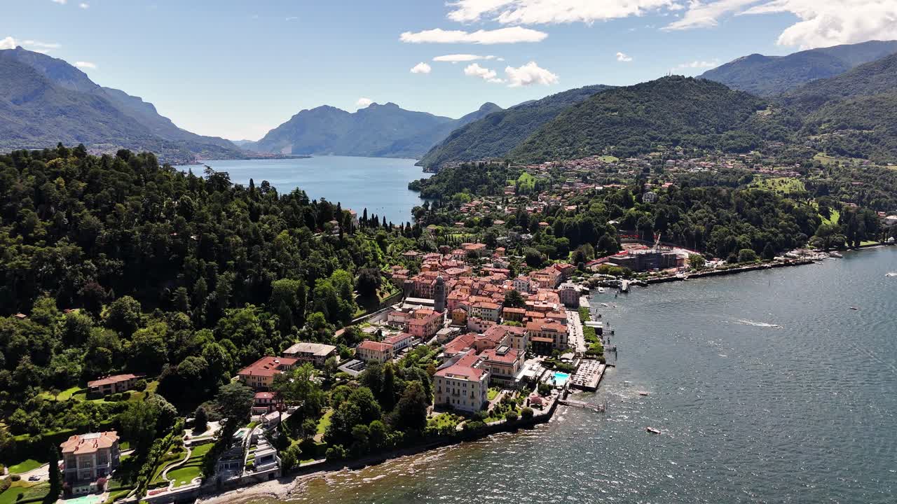 Aerial view of Bellagio in Lago di Como Italy with its waterfront village, red-roofed buildings, lush hills and expansive lake surrounded by mountain ridges under a bright clear sky