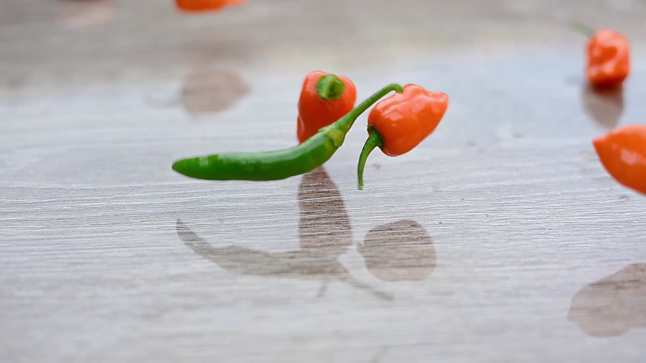 A slow-motion scene of habanero peppers rolling across a kitchen table.